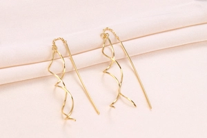 Close-up of golden spiral pull-through earrings on elegant soft pink fabric background