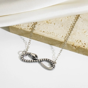 Gothic silver snake bracelet shaped as an infinity symbol on a beige stone background