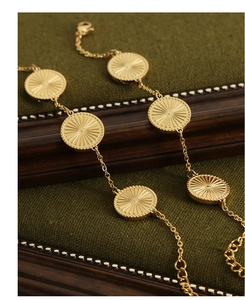 Detail of gold titanium steel bracelet with textured round coin pendants on green fabric