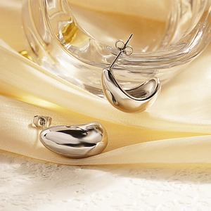 Polished silver stainless steel C-shaped crescent stud earrings on soft cream fabric