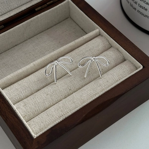 Elegant silver bow stud earrings presented in a luxury wooden jewelry box