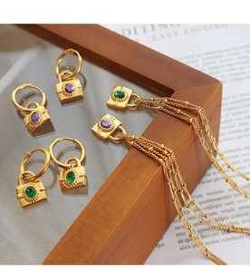 Detail of gold padlock earrings with green and purple zircon gems on a glass surface