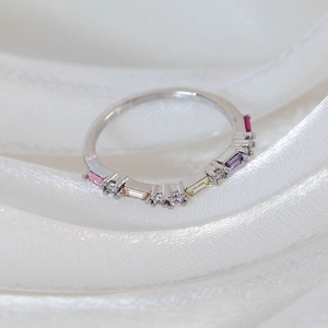 Macro detail of silver ring with rainbow pavé zircon stones on a white silk ribbon