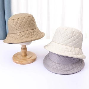 Close-up of quilted bucket hats in khaki, beige, and grey on wooden stands