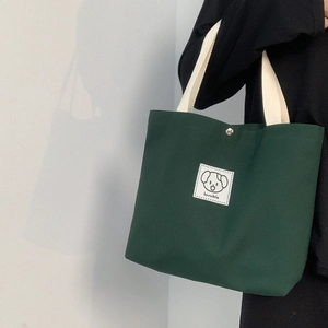 Detail of dark green canvas tote bag with lovable cartoon dog patch held by a model