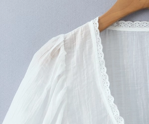Détail d'un haut blanc col V montrant la dentelle délicate et le tissu plissé texturé