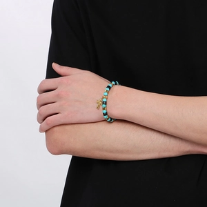 Gros plan du bracelet de perles turquoise bohème avec pendentif croix dorée au poignet