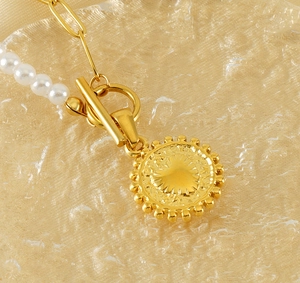 Macro shot of gold sun totem pendant with pearl chain and T-bar toggle clasp detail