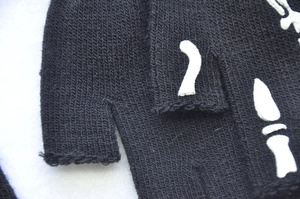 Macro shot of knitted fingerless gloves featuring a white skeleton hand bone pattern