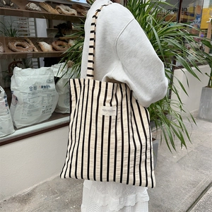Detail of the black and white striped canvas tote bag showing wide shoulder strap and fabric label