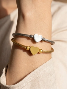Close-up of gold and silver heart charms on woven stainless steel wire bracelets
