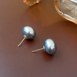 Detailed view of high-luster dark grey pearl earrings on premium brown leather surface