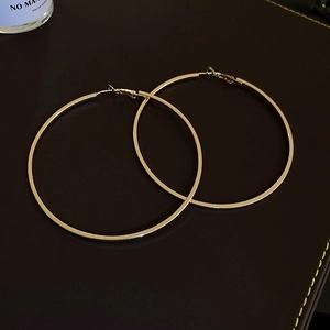 Close-up of large gold geometric hoop earrings on dark leather background with props