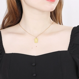 Detail of a gold 18k square zodiac pendant necklace worn by a model on a black top