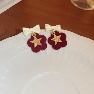 Dettaglio di orecchini a fiore rossi con fiocco bianco e stella d'oro su piatto retrò