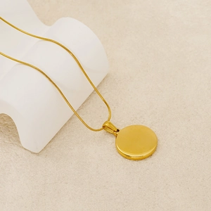 Detailed view of a gold zodiac pendant necklace with a sleek snake chain on beige surface