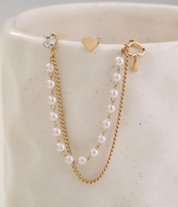Detail of gold heart earrings set with pearls, crystal studs and layered tassel chains