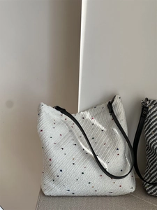 Macro shot of white tweed tote bag with colorful specks and black leather strap
