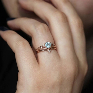 Close-up of rose gold crown ring set with round blue gemstone and V-shaped band on finger