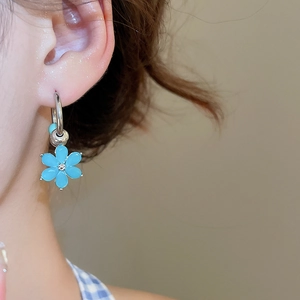 Silver-plated hoop earring with blue floral pendant and metal bead on model's ear