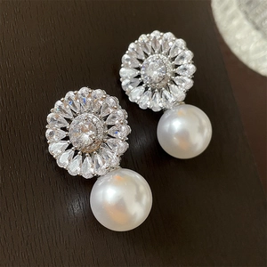 Macro view of flower-shaped zircon earrings with elegant white drop pearls on wood