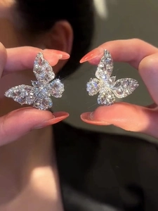 Detailed close-up of sparkling butterfly earrings with clear zircons held in hands