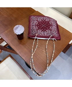 Detail of red paisley canvas tote bag with colorful beaded shoulder strap on wooden desk