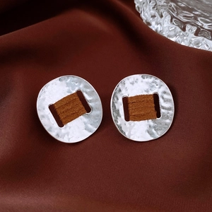 Detail of silver textured earrings with brown leather wrap on silk fabric