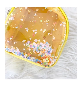 Detail of yellow transparent PVC waist bag with colorful sequins on white faux fur background