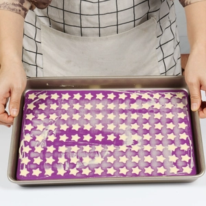 Detail of purple batter in non-stick metal mold with white star patterns for baking