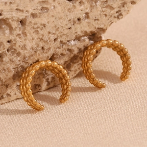 Détail macro de boucles d'oreilles C dorées à trois rangées de perles sur fond de pierre