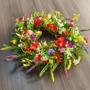 Close-up of a colorful faux floral wreath with red, purple, and yellow flowers on grey wood