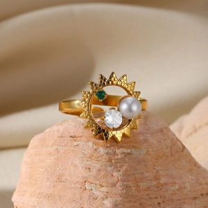 Detail shot of a gold starburst ring with pearl and green gemstone on a natural rock