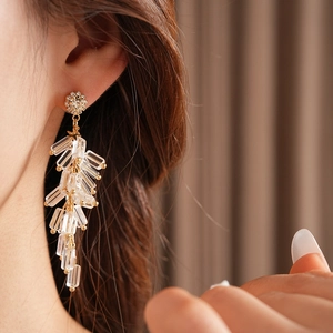 Detail of long gold earrings with wheat ear crystals worn by model in soft lighting