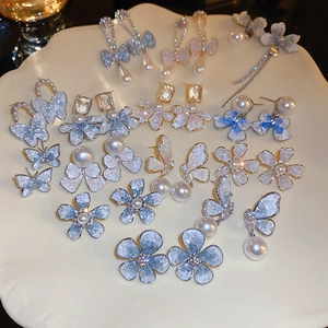 Flat lay of floral and butterfly earrings with faux pearls and crystals on a tray
