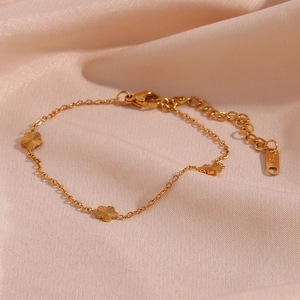 Detail of 18K gold plated bracelet with flower pendants on soft pink silk background