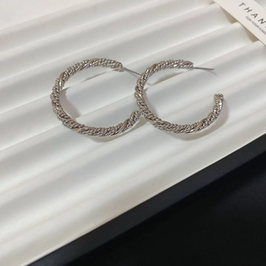 Close-up of silver C-shape earrings with twisted rope texture on a white display stand