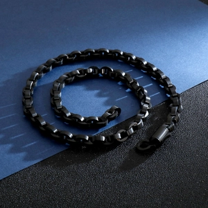 Close-up of a minimalist black stainless steel chain necklace on a textured blue background