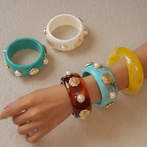 Detail of wide resin bangles with gold shell reliefs and inlaid faux pearls on stone surface