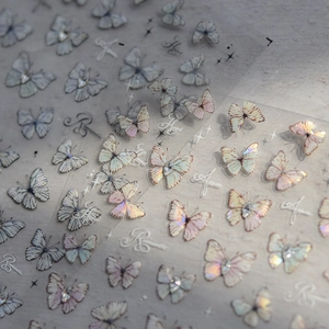 Macro shot of 3D crystal butterfly nail decals with iridescent finish and pearl accents