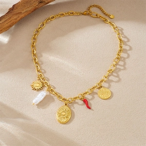 Collana vintage dorata con medaglione sole, perla e ciondolo peperoncino su sfondo sabbioso