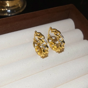 Macro shot of gold-tone hollow Cuban chain hoop earrings set with sparkling zircons