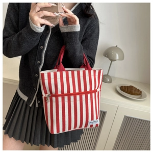 Detail of red and white striped canvas tote bag showing the front zipper pocket and handle