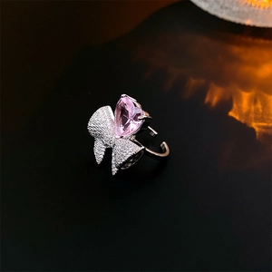 Gros plan sur bague en argent avec pierre coeur rose et nœud en diamant scintillant