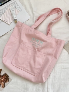 Pink canvas tote bag with blue bow embroidery and long shoulder straps on white bedding