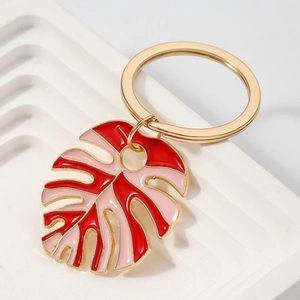 Golden monstera leaf keychain with red and pink enamel finish on white stone tray