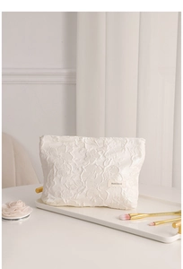 Detail of white embossed floral jacquard makeup bag on tray with soft lighting