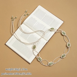 Détail d'une chaîne de taille tressée bohème avec pierres vertes sur un fond de livre ancien