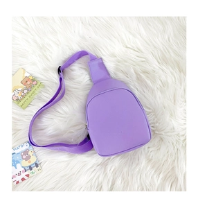 Detail view of a small purple PU leather crossbody bag on a white plush background