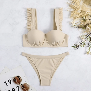 Flat lay detail of beige two-piece bikini with ruffled straps on marble background